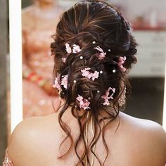 the back of a woman's head with pink flowers in her hair and pearls in her hair