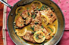 a pan filled with meat and lemons on top of a red table cloth next to a fork