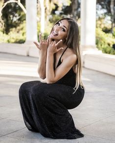 a woman sitting on the ground with her hand up in front of her face and smiling