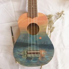 a ukulele sitting on top of a white sheet next to a pen and flower