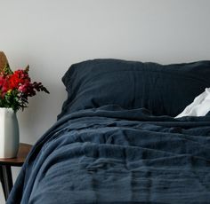 a bed with a blue comforter next to a white vase filled with red flowers