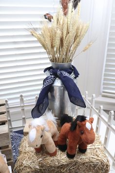 three stuffed horses sitting on top of a hay bale in front of a window