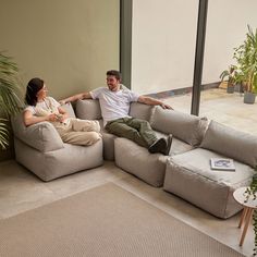 a man and woman sitting on couches facing each other in front of large windows