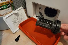 a person is opening the door to a washing machine with an orange tray on it