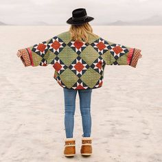 a woman standing in the sand with her back to the camera wearing a quilted jacket and hat