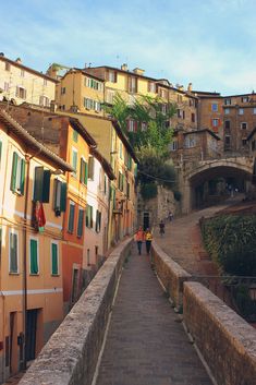 a narrow street with buildings on both sides and people walking up the stairs to it