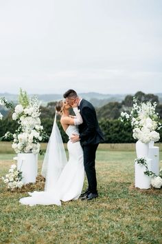 a bride and groom kissing in front of their wedding ceremony archs with white flowers