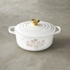 a white casserole with flowers painted on the side and a gold lid sits on a gray surface