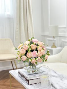 a glass vase filled with pink roses on top of a marble coffee table in a living room