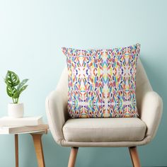 a white chair with a colorful pillow on it next to a potted green plant