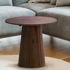 a round wooden table sitting on top of a hard wood floor next to a couch