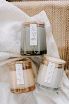 three candles sitting on top of a bed next to a white blanket and pillows with tags