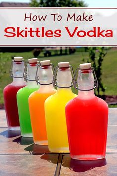 four bottles with different colored liquids in them on a wooden table outside near grass and trees