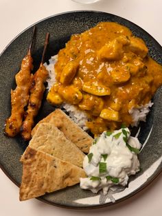 a black plate topped with rice, meat and veggies next to crackers