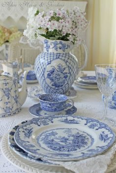 a blue and white table setting with flowers in a vase, china dishes and glasses