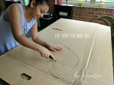 a woman is cutting out a cardboard box with scissors and glue on the bottom half