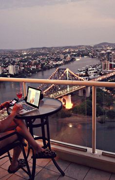 a woman sitting at a table on top of a balcony with a laptop computer next to her