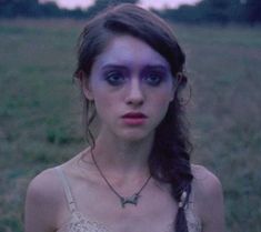 a woman with blue makeup standing in a field looking at the camera while wearing a bra