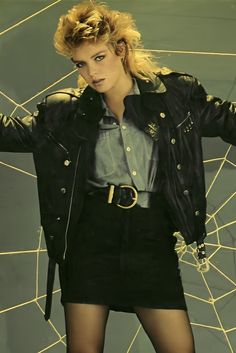 a woman with blonde hair wearing a black jacket and skirt, standing in front of a spider web