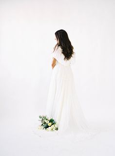 a woman in a white dress is standing with her back to the camera and holding a bouquet of flowers