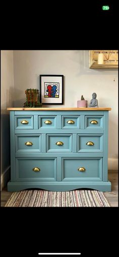 a blue dresser with gold knobs in the middle and an image above it on top