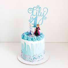 a frozen princess cake with blue frosting and two figurines sitting on top