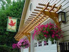 a wooden pergolan with flowers hanging from it's sides next to a garage