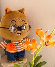 a teddy bear wearing glasses and holding a carrot in front of a plant with orange flowers