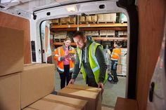 two men in yellow vests are loading boxes into the back of a moving truck