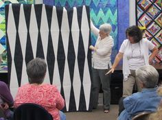 several people are looking at quilts on display in a room full of older women