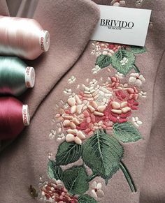 some spools of thread sitting on top of a pink jacket with flowers and leaves