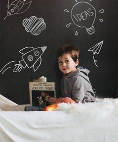 a young boy sitting on top of a bed next to a blackboard with drawings