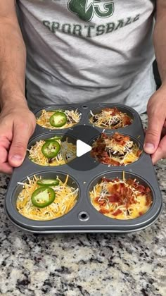 a person holding a muffin tin filled with mini pizzas and cheese toppings