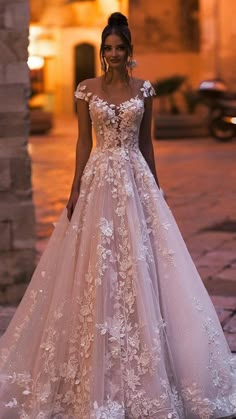 a woman wearing a wedding dress with flowers on the skirt and off the shoulder, standing in