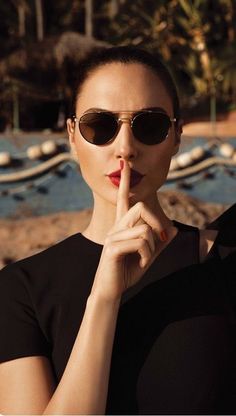 a woman in black shirt and sunglasses holding her finger up to her lips with both hands