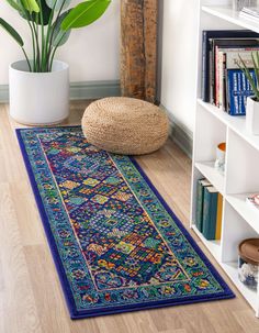 a blue rug on the floor next to a potted plant and bookshelf