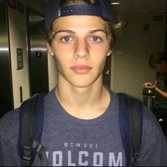 a young man wearing a hat and backpack in an elevator with his hand on his hip