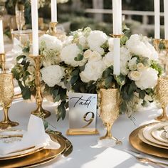 gold mirror table numbers for wedding on a white table white flowers and gold plates Elegant White And Gold Wedding Decor, Classy Wedding Flower Arrangements, Tall Flowers Wedding Table, Brass Wedding Table Decor, Dark Green And Gold Table Setting, Classic Wedding Tablescape, Classy Wedding Ideas Decor, Elegant Classy Wedding Decor, Glamour Wedding Decorations