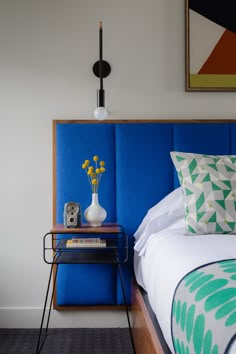 a bed with blue headboard and pillows on it next to a table with yellow flowers