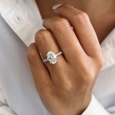 a woman's hand with a diamond ring on her left hand and a white shirt on the right