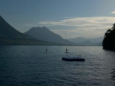 two people stand on their surfboards in the middle of a body of water with mountains in the background