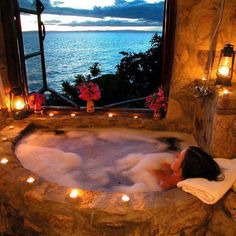 a woman laying in a hot tub with candles on the side and water behind her