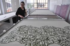 a woman is standing in front of a large screen print on a table with windows behind her