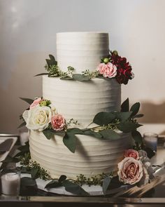 a three tiered cake with flowers and greenery on the top is ready to be cut