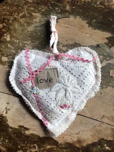 a white heart hanging on a wooden table with the word love written on it and a pink ribbon