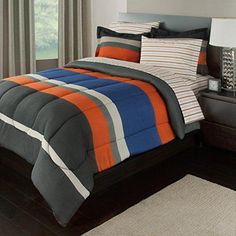 a bed with orange, blue and grey comforter in a bedroom next to a window