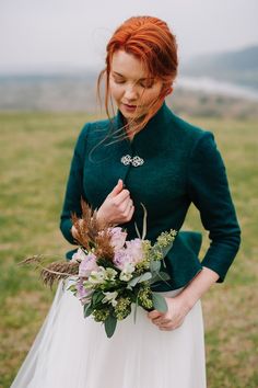 a woman wearing a green jacket holding a bouquet of flowers and greenery in her hands