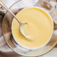 a glass bowl filled with yellow liquid on top of a white table cloth and wooden spoon