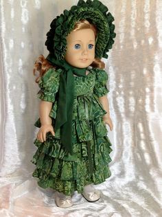 a doll wearing a green dress and bonnet with leaves on it's head, standing in front of a white backdrop