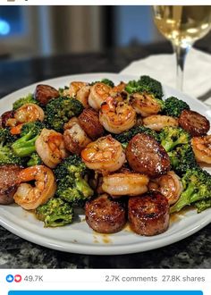 a white plate topped with shrimp and broccoli next to a glass of wine